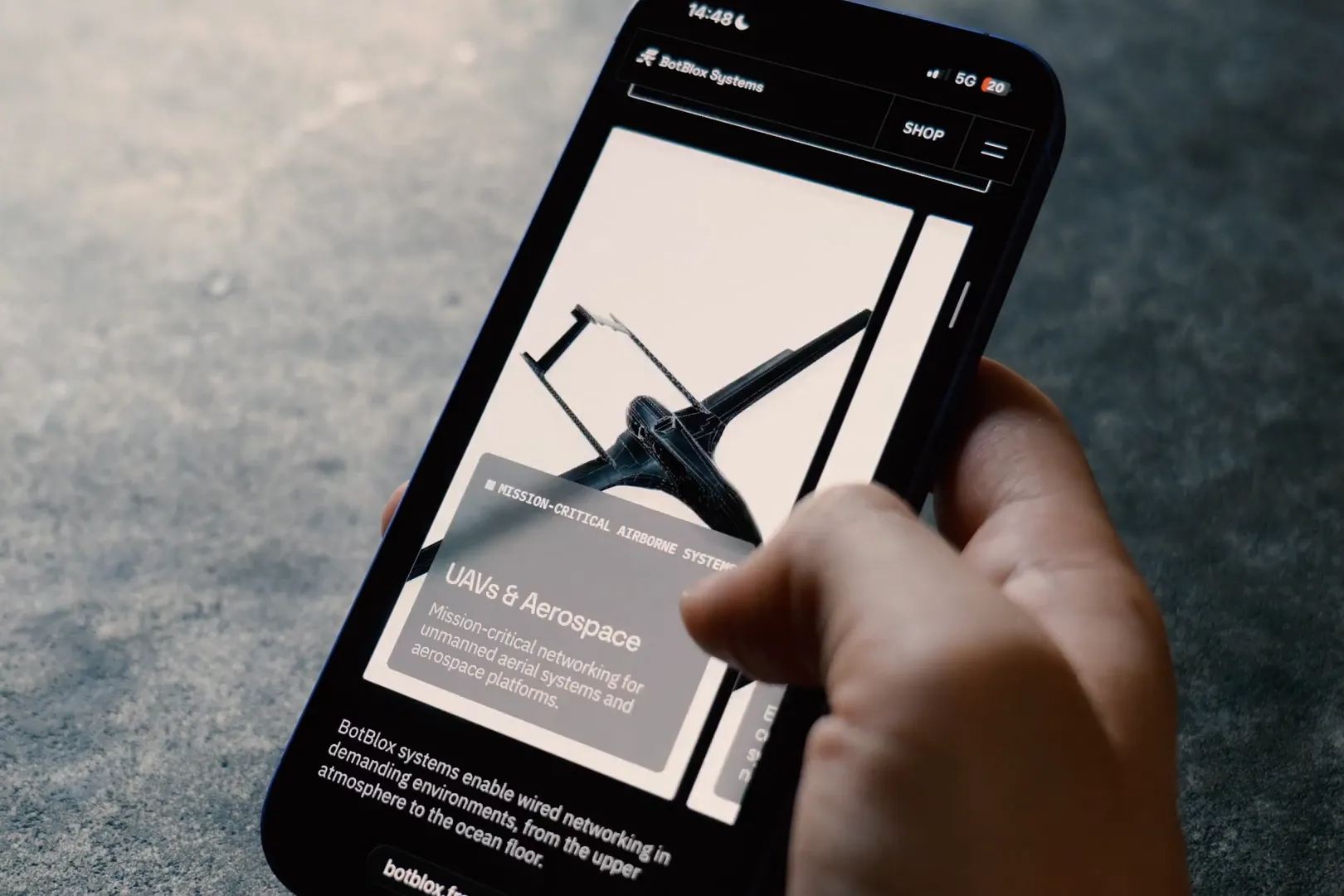 Hand holding a smartphone on the BotBlox Systems website, UAVs and aerospace page, designed by Junca Studio
